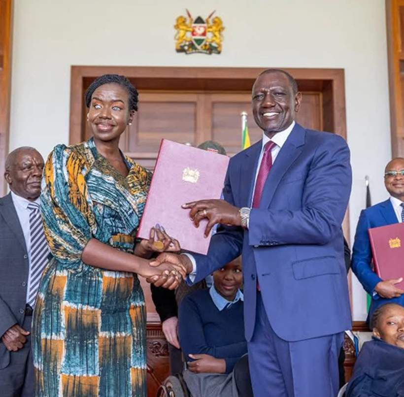 Kenya’s President William Ruto hands over the Persons with Disabilities Act 2025 to Senator Crystal Asige, who is visually impaired, after signing the bill into law at State House, with officials and persons with disability in the background.