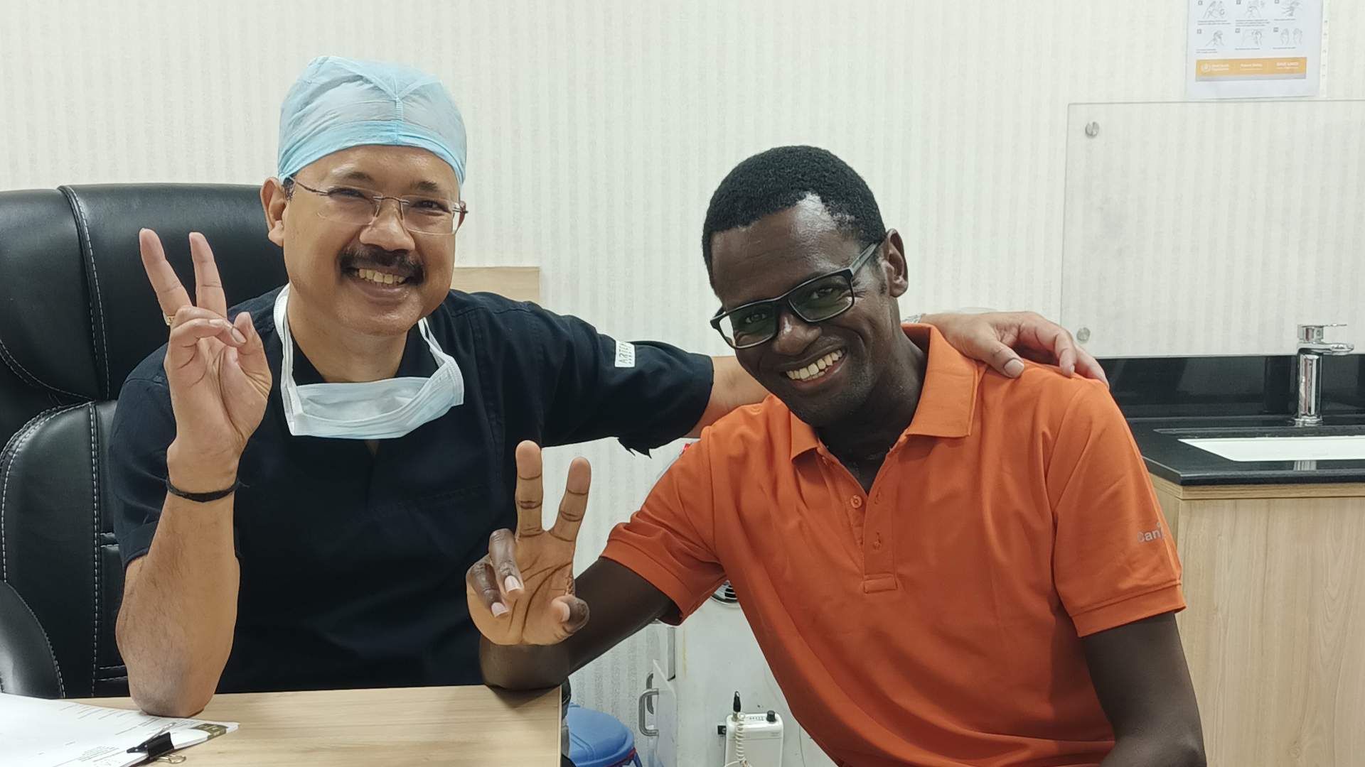 Dr. Biswajyoti Hazarika, Chief of Head and Neck Surgery at Artemis Hospital, and his patient Kizito Namulanda, who has recovered from a partial laryngectomy, pose together outside Artemis Hospital; in-set shows them smiling inside a clinic room.